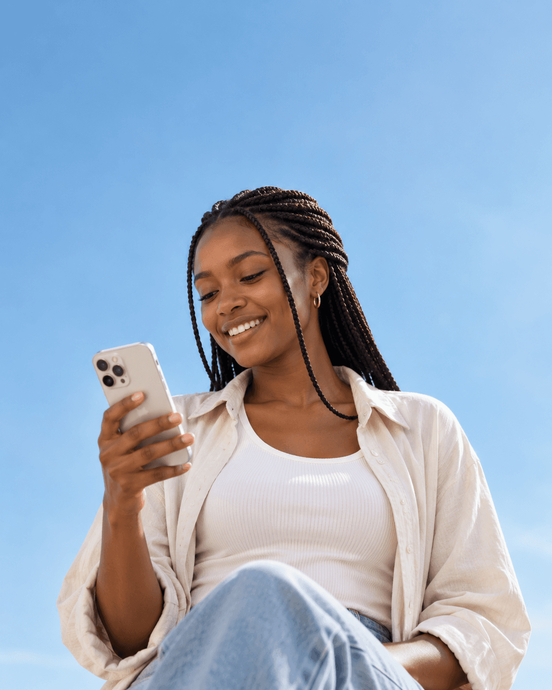 A woman smiling at her phone against a blue sky